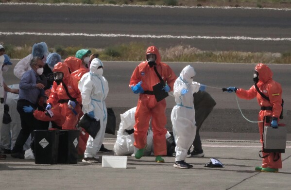 Passengers are sprayed with disinfectant by Spanish government officials before boarding a plane after disembarking from the hantavirus-stricken cruise ship MV Hondius at Tenerife airport in the Canary Islands, Spain, Sunday, May 10, 2026. (AP Photo/Arturo Rodriguez)