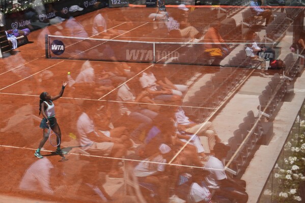 Fans are reflected in a glass partition as Coco Gauff, of the United States, serves the ball to United States' Iva Jovic during their match at the Italian Open tennis tournament in Rome, Monday, May 11, 2026. (AP Photo/Alessandra Tarantino)