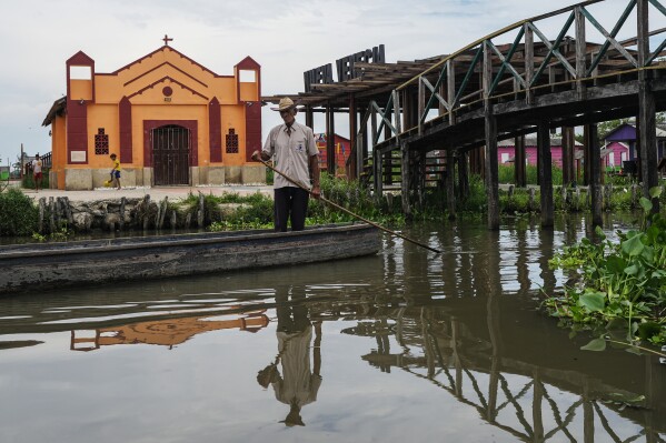A man navigates near an invasive plant called a water hyacinth, also known as Eichhornia, in front of a church Thursday, April 30, 2026, in Nueva Venecia, Colombia, where dozens of people were killed by illegal armed groups on November 22, 2000. (AP Photo/Ivan Valencia)
