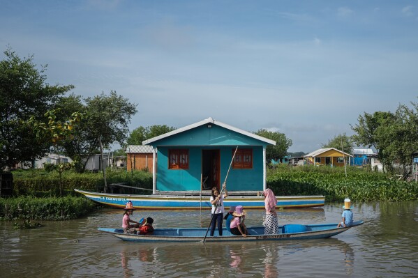 The children are transported by boat to go to school near homes surrounded by an invasive plant species called water hyacinth plant, also known as Eichhornia crassipes, Thursday, April 30, 2026, in Buenavista, Colombia. (AP Photo/Ivan Valencia)