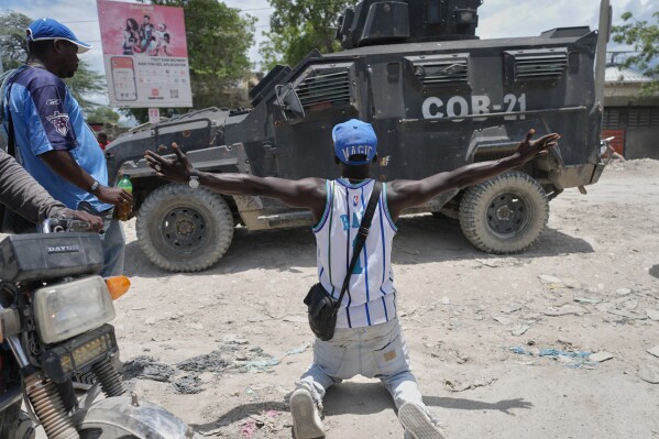 A resident of Cité Soleil kneels before a police armored vehicle and demands that the police go and fight the gangs that control their neighborhood, in Port-au-Prince, Haiti, Tuesday, May 12, 2026. (AP Photo/Odelyn Joseph)