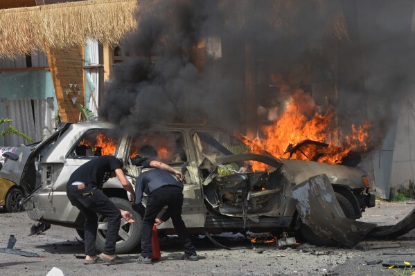 A person is seen inside a burning vehicle as men attempt to put out the fire after an Israeli airstrike hit a car in the coastal town of Barja, south of Beirut, Lebanon, Wednesday, May 13, 2026. (AP Photo/Mustafa Jamalddine)