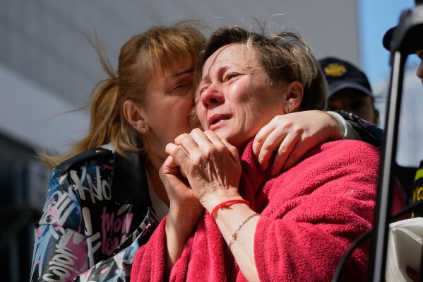 A neighbour hugs a crying woman at a site of a Russian missile attack on a residential building in Kyiv, Ukraine, Thursday, May 14, 2026. (AP Photo/Efrem Lukatsky)
