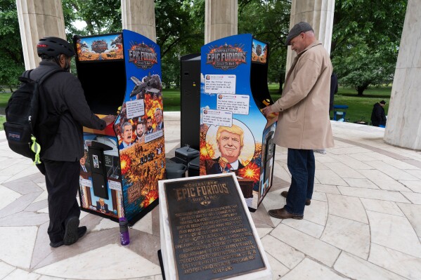 District of Columbia resident Malcom Jones, right, plays a video game mocking the war on Iran, at the DC War Memorial on the National Mall, Monday, May 11, 2026, in Washington. (AP Photo/Manuel Balce Ceneta)
