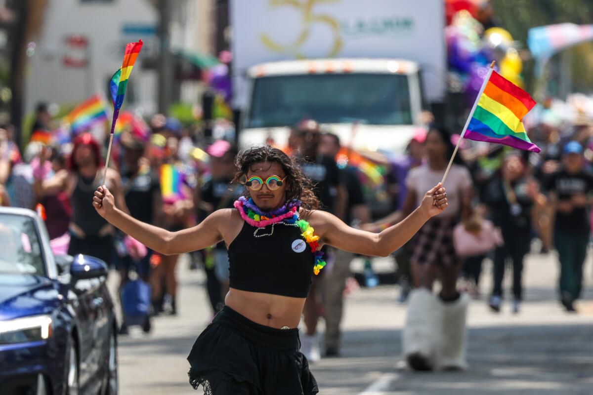 A marcher holds up two rainbow flags.