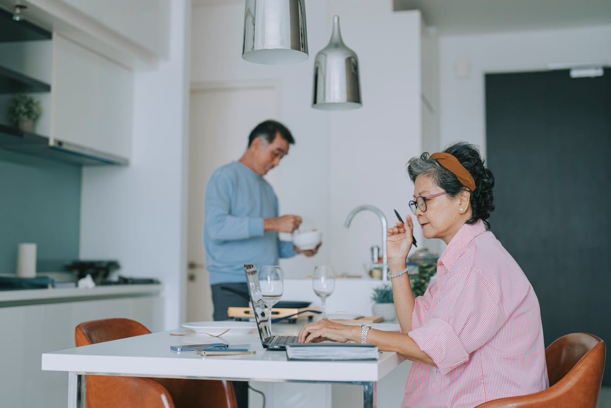 Couple in kitchen together, one using a laptop.