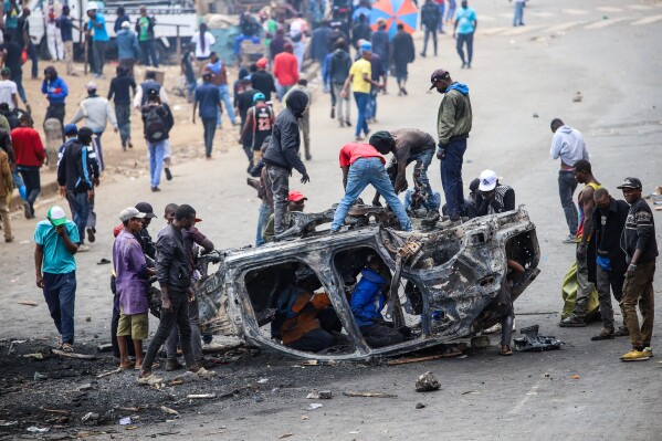 People strip parts from a burned-out vehicle during a public transport strike over fuel prices in Nairobi, Kenya, Monday, May 18, 2026. (AP Photo/Patrick Ngugi)