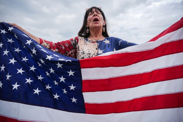 Kathy Fain, from Longview, Texas, holds an American flag while singing the National Anthem during Rededicate 250, a mostly conservative Christian prayer gathering in honor of the United States' 250th anniversary, on the National Mall, Sunday, May 17, 2026, in Washington. (AP Photo/Julia Demaree Nikhinson)