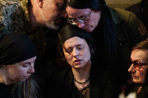 A mother mourns sitting by the coffins of her daughters Liubava and Vira Yakovleva, killed by a Russian rocket strike on a residential building earlier this month, during their funeral, in Kyiv, Ukraine, Tuesday, May 19, 2026. (AP Photo/Evgeniy Maloletka)