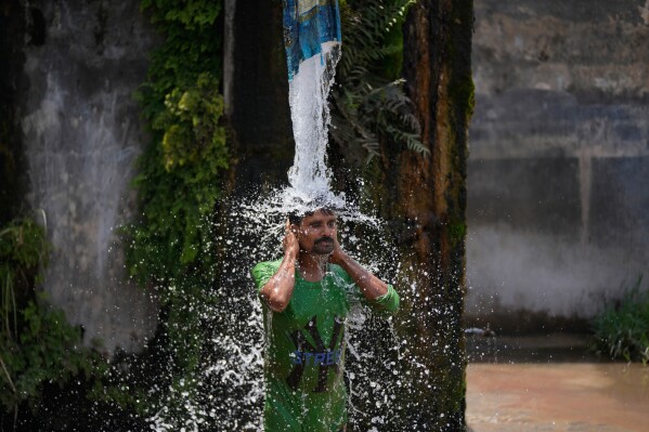 A man bathes from a roadside water tap to cool himself on a hot summer day on the outskirts of Jammu, India, Tuesday, May 19, 2026. (AP Photo/Channi Anand)