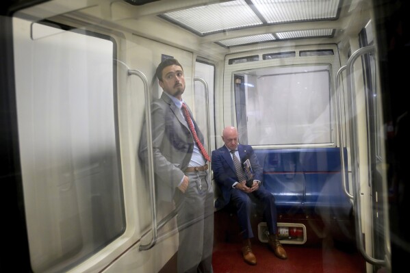 Sen. Mark Kelly, D-Ariz., seated, checks his phone while riding a train in the Senate subway at the Capitol, Tuesday, May 19, 2026, in Washington. (AP Photo/Rod Lamkey, Jr.)