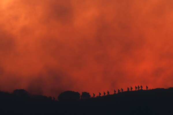 Firefighters are silhouetted walking amid the firing operation to control the Sandy Fire, Tuesday, May 19, 2026, in Simi Valley, Calif. (AP Photo/Caroline Brehman)