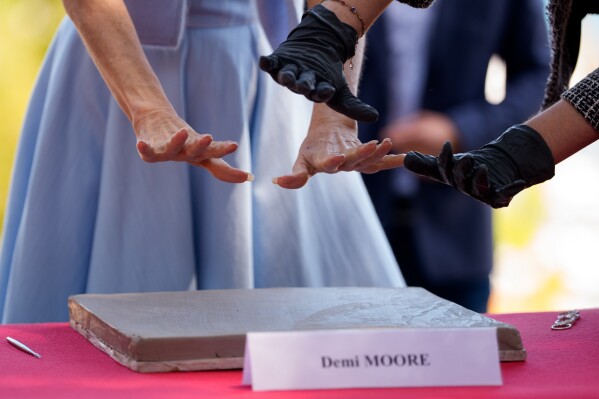Jury member Demi Moore, left, places her hands in clay at the photo call for the signing of the city of Cannes Golden Book and Handprint ceremony at the 79th international film festival, Cannes, southern France, Wednesday, May 20, 2026. (AP Photo/Andreea Alexandru)