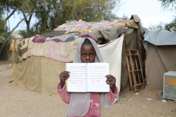 Sudanese student Magdah Abu Kassem, 12, who left Sudan with her family during the civil war, poses with her notebook in front of her class room at a refugees school for children, in Tajoura, east Tripoli, Libya, Monday, May 18, 2026. (AP Photo/Yousef Murad)