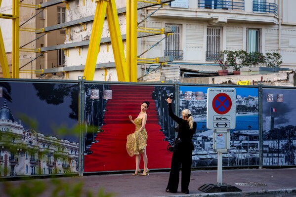 A woman poses for a photographer in front of a poster showcasing the famous red carpet during the 79th international film festival, Cannes, southern France, Thursday, May 14, 2026. (AP Photo/Andreea Alexandru)