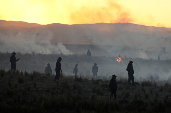 Anti-government protesters standing in a field are silhouetted against clouds of tear gas launched by police, near El Alto, Bolivia, Saturday, May 16, 2026. (AP Photo/Juan Karita)