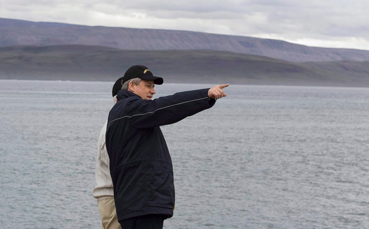 A man stands with another person by a large body of water, pointing.
