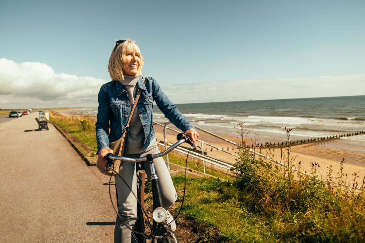 Smiling person riding bicycle by the ocean.