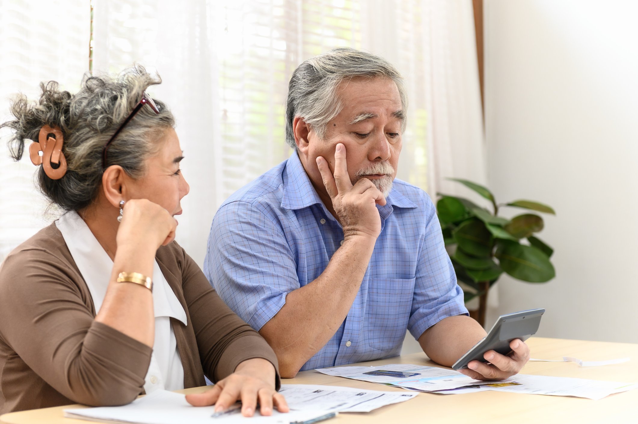 A visibly worried couple examining bills and financial statements while seated at a table in their home.