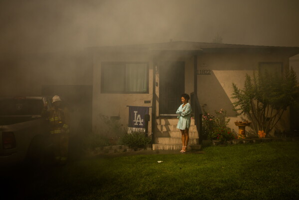 Veronica Smith watches from her doorstep as firefighters battle a commercial structure fire in South Gate, Calif., on Sunday, May 24, 2026. (AP Photo/Ethan Swope)