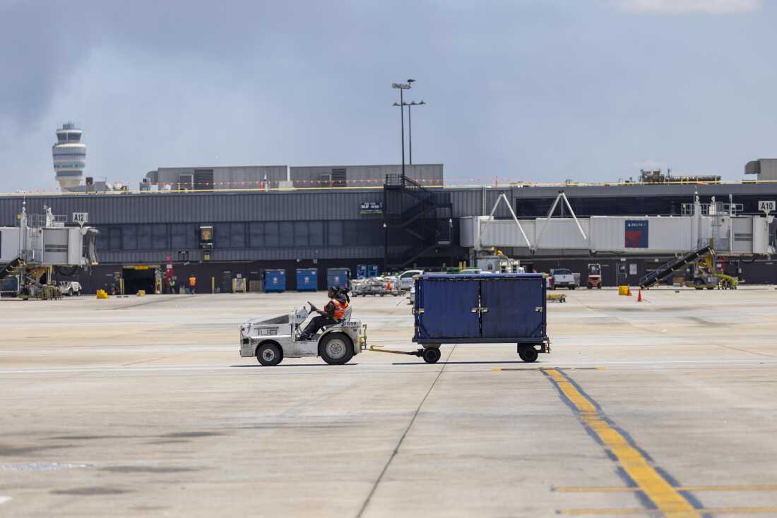 A Delta Air Lines employee drives an aircraft tug with a luggage cart on the tarmac at Atlanta Hartsfield Jackson International Airport.