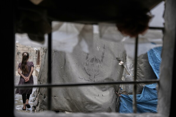 A girl walks through al-Karama camp, established in the early years of the Syrian conflict and built from scratch with light-brick structures covered with fabric to house internally displaced Syrians near the village of Atmeh, Idlib province, Syria, Tuesday, May 19, 2026. (AP Photo/Omar Albam)