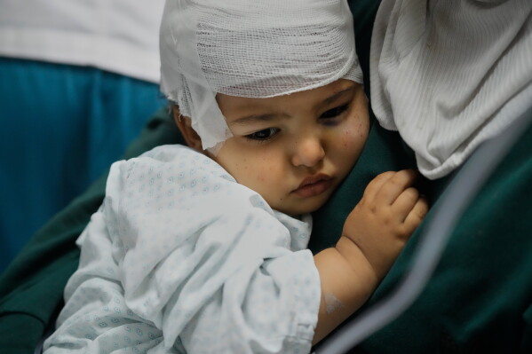 Ali Al-Aqleh, 18 months, rests in the arms of his mother, Hayat Al-Aqleh, at Jabal Amel Hospital in the southern port city of Tyre, Lebanon, Wednesday, May 27, 2026, after undergoing head surgery for injuries sustained in an Israeli airstrike a day earlier in the village of Charnay near Tyre. (AP Photo/Mohammad Zaatari)