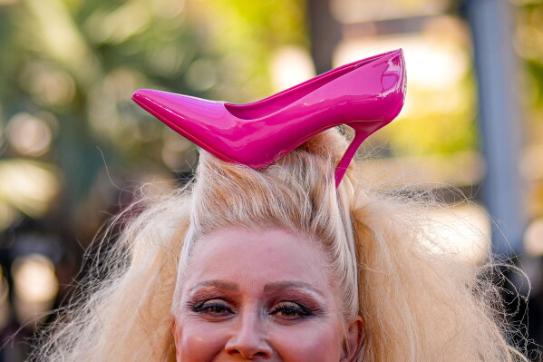 Elena Lenina smiles as she walks on the red carpet with a shoe in her hair at the premiere of the film 'Karma' at the 79th international film festival, Cannes, southern France, Friday, May 15, 2026. (AP Photo/Andreea Alexandru)