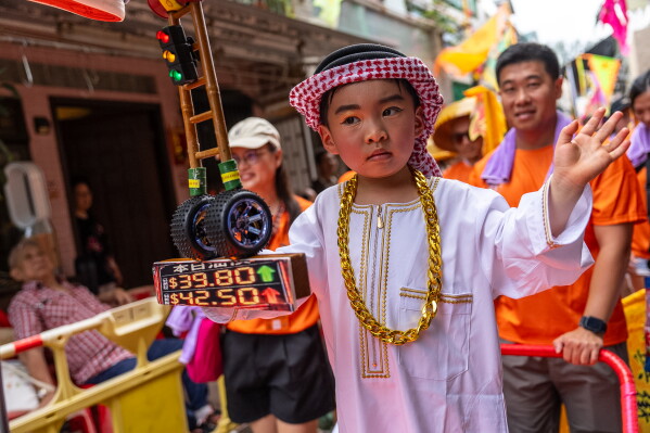 A child participates in the Piu Sik Parade with a replica gas station price sign model at the Bun Festival in Cheung Chau Island in Hong Kong, Sunday, May 24, 2026. (AP Photo/Chan Long Hei)