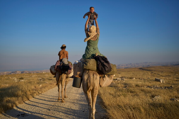 Israeli settler parents travel with their baby on camels in the northern Judean Desert near the settlement of Kochav Hashachar, in the West Bank, Monday, May. 25, 2026. (AP Photo/Ohad Zwigenberg)