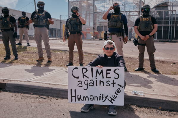 A protester holds a sign as ICE agents stand guard outside the Delaney Hall detention during a protest against the transfer of detainees on Tuesday, May 26, 2026, in Newark, N.J. (AP Photo/Andres Kudacki)