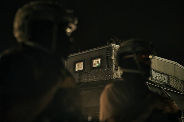 A detained migrant has a laser pointed at him as he stands by the window while ICE agents stand guard outside the Delaney Hall detention center during a protest near the entrance gates, Wednesday, May 27, 2026, in Newark, N.J. (AP Photo/Andres Kudacki)