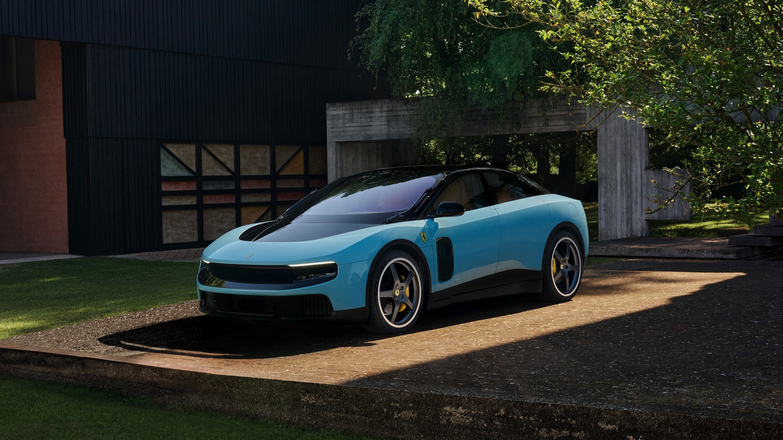 A sleek, modern light blue sports car with black accents is parked on a sunlit concrete platform next to a dark building and surrounded by greenery.