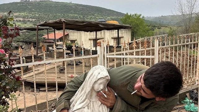 A soldier smokes and pushes another cigarette onto the mouth of a statue of the Virgin Mary in Debel, Lebanon, in this pictur