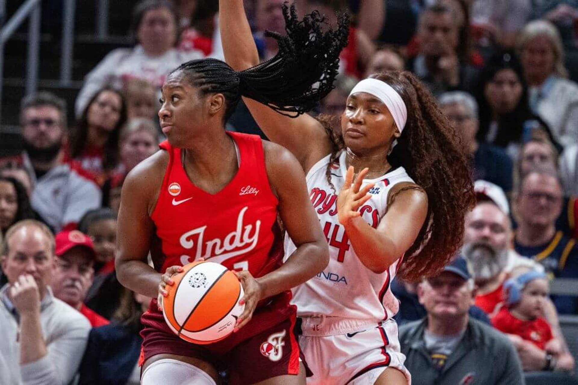 Indiana Fever center Aliyah Boston looks to her right while holding a basketball in both hands as Washington Mystics forward Kiki Iriafen defends.