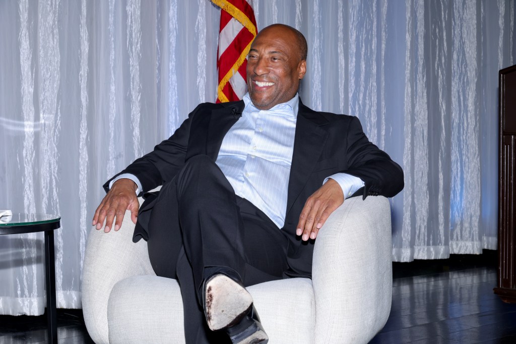 Byron Allen smiling while seated in an armchair.