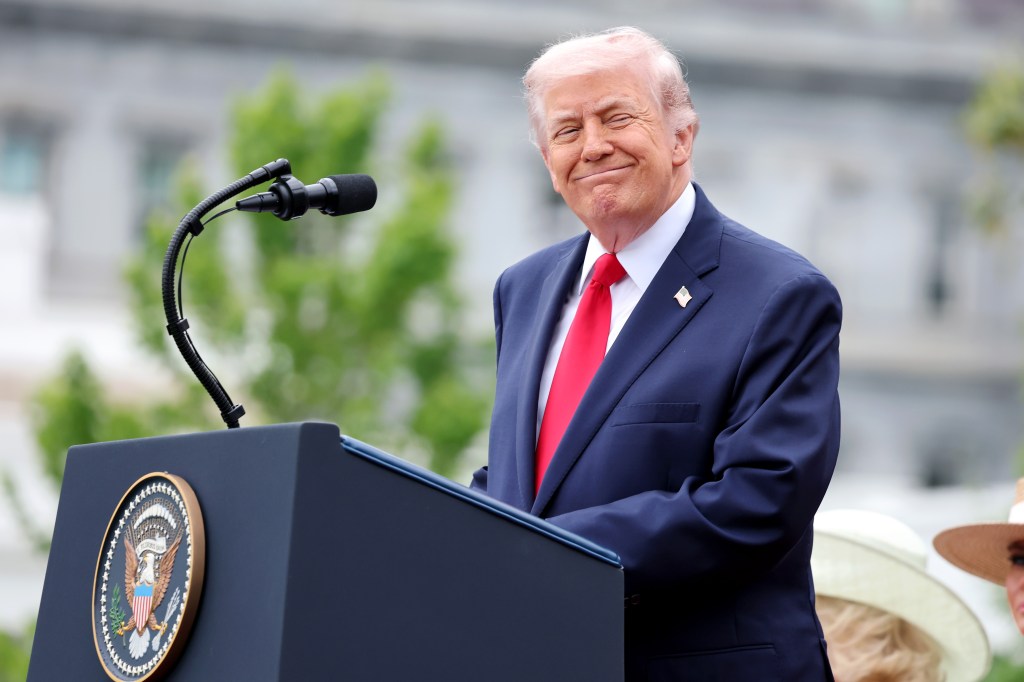 President Donald Trump smiling while giving a speech at a podium on the South Lawn.