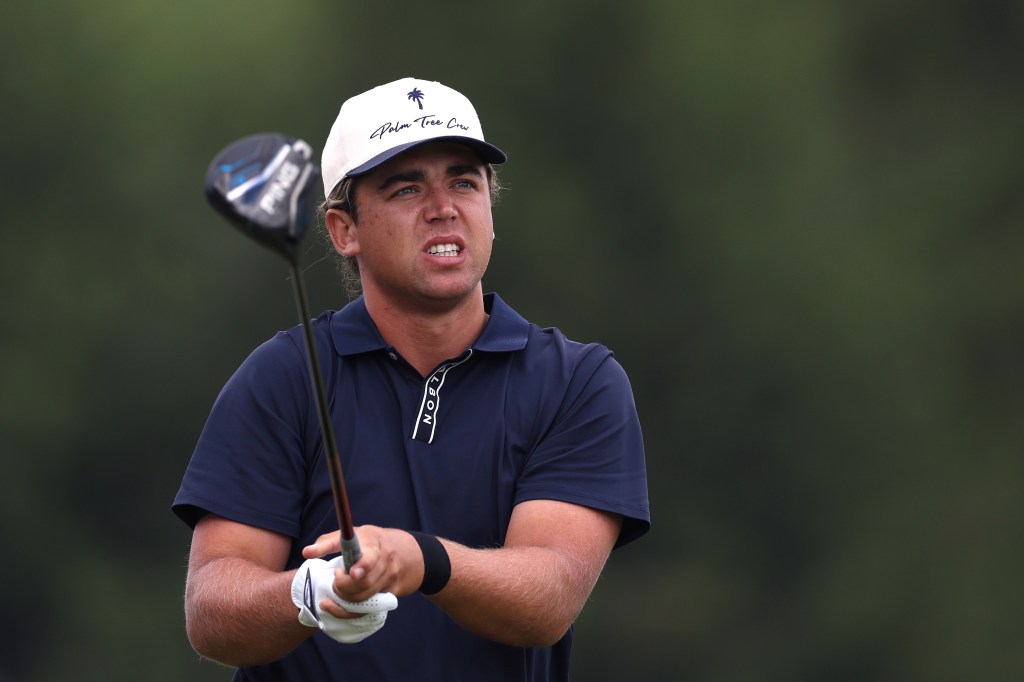A male golfer wearing a white and navy blue cap with a palm tree logo, looking intensely to his right.