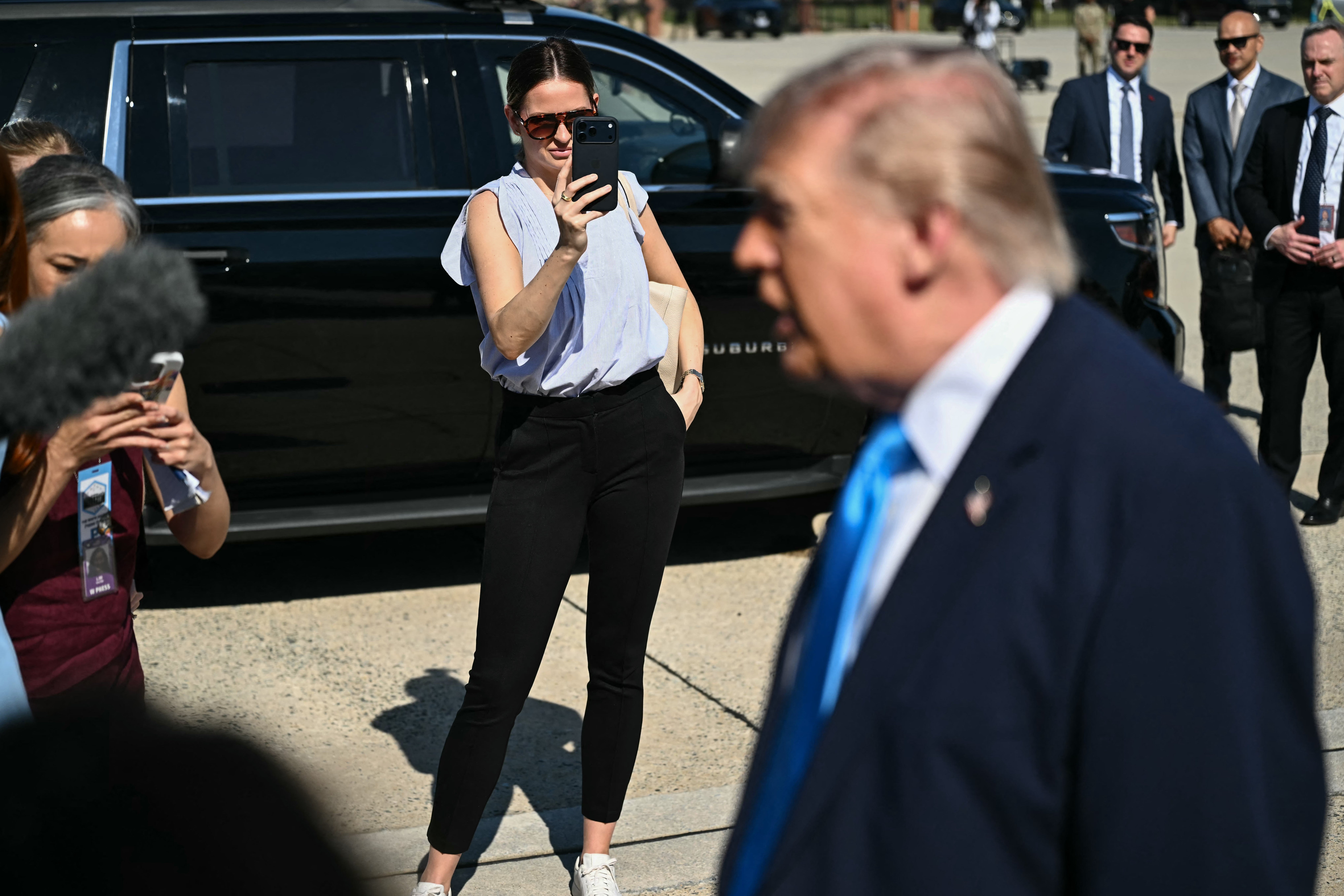 Margo Martin, Special Assistant to the President and Communications Advisor, takes video on her phone as US President Donald Trump speaks to reporters before boarding Air Force One at Joint Base Andrews, Maryland