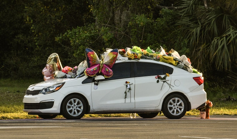 A white sedan, covered in mylar balloons and flower bouquets, at sunset.