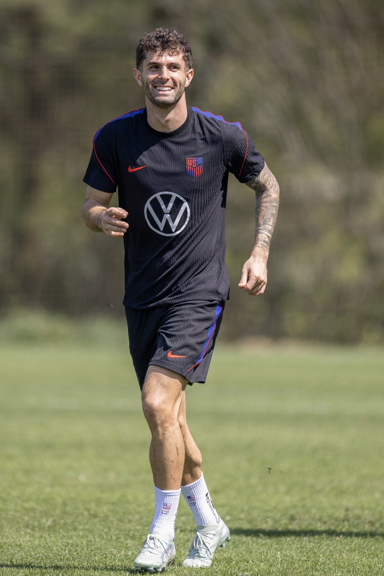 Christian Pulisic smiles while jogging on a practice field.
