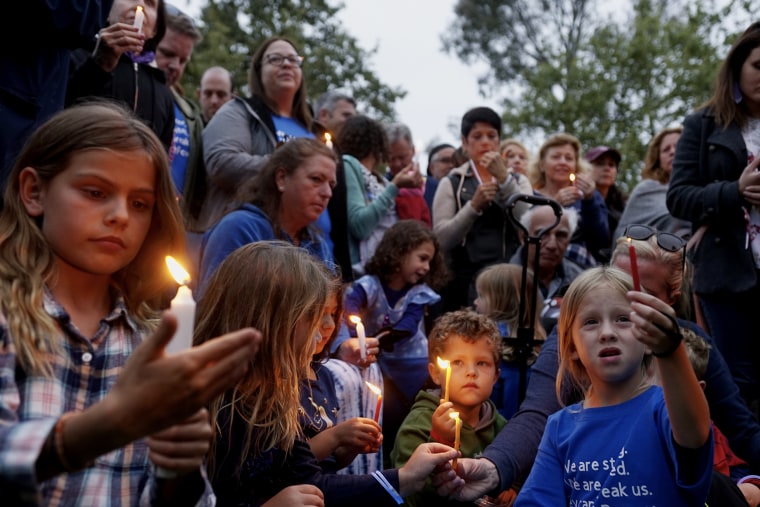 Several children, with adults in the background, at a candlelight vigil at dusk.
