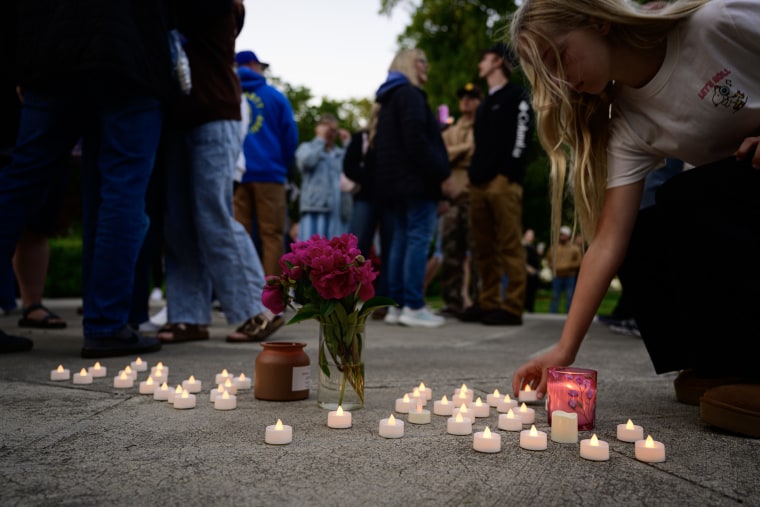 A young woman places an electric candle down among dozens of others at a makeshift memorial.