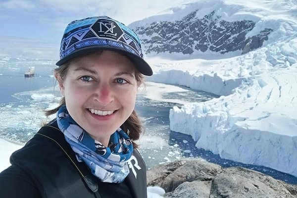 A woman wearing a cap stands in front of any icy frontier.