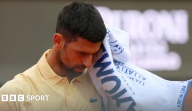 Novak Djokovic reacts during the Italian Open, raising a towel to his face while wearing a yellow tennis shirt