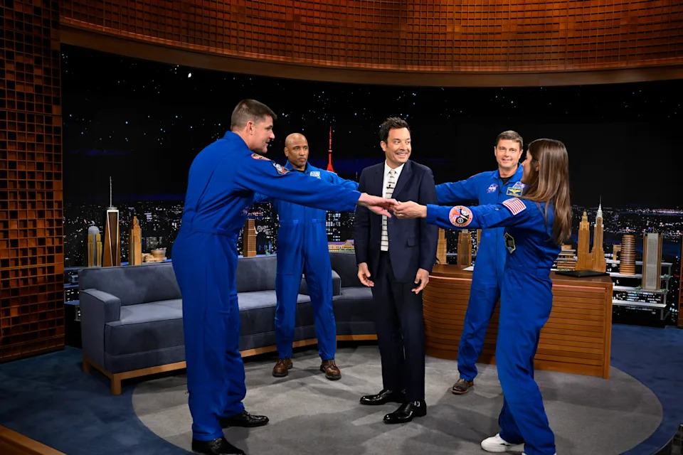 The Artemis II crew members hold hands and form a circle around Jimmy Fallon.