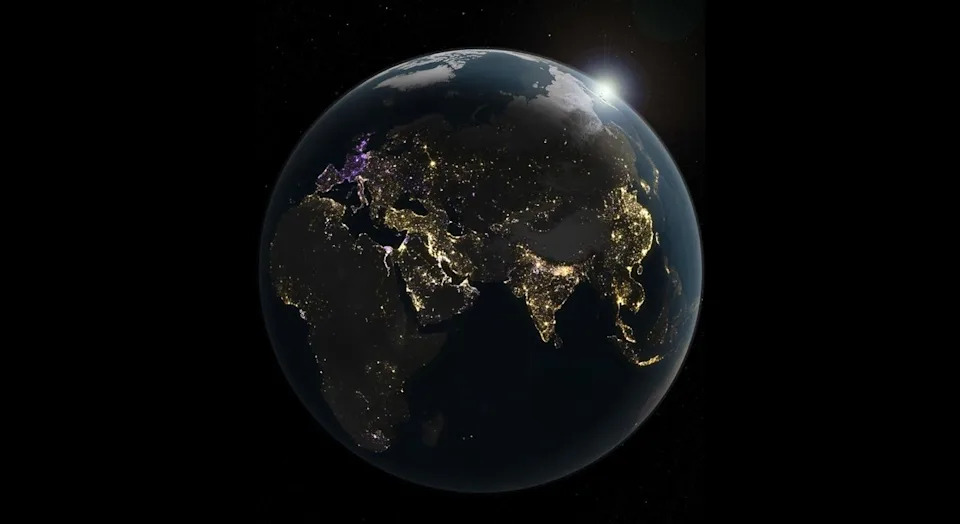 An illustration of earth at night. the planet is mostly black and in shadow, revealing patterns of dots of light tracing the outlines of continents.