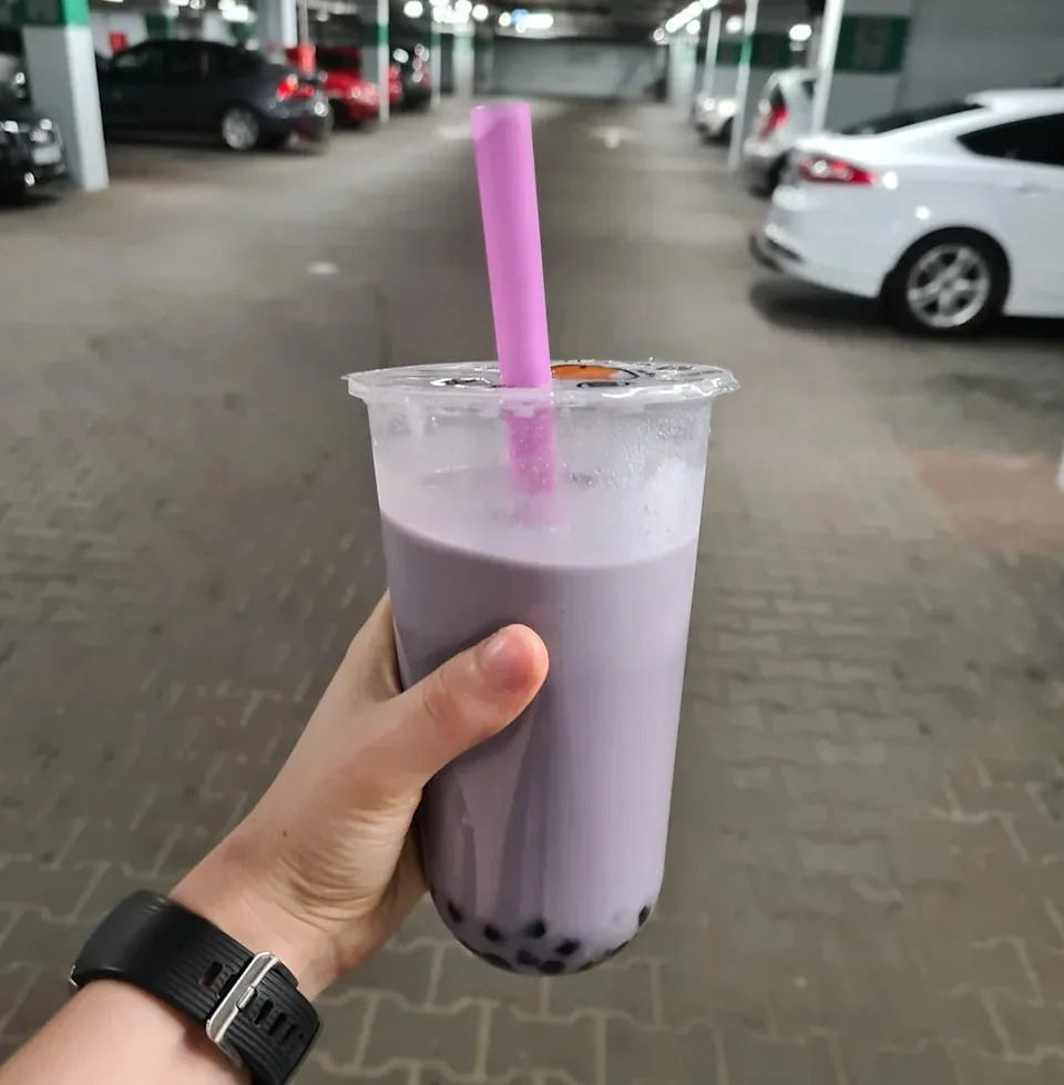 Hand holding a cup of bubble tea with a straw, in a parking garage setting