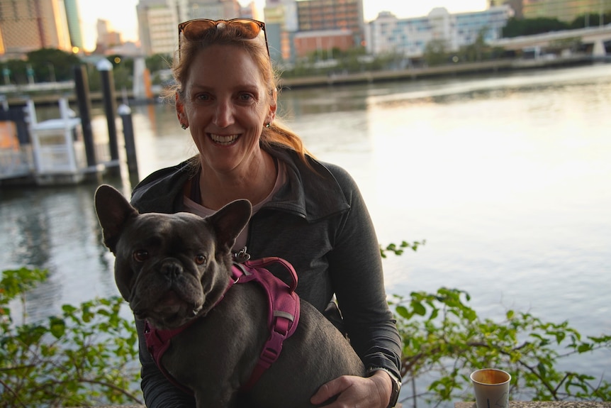 A woman sits with a dog on her lap with the Brisbane River in the background.