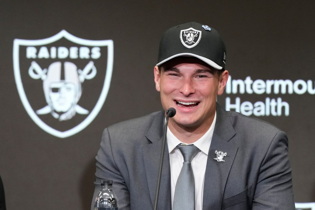 Fernando Mendoza, a football player, wearing a suit and Raiders cap, smiles into a microphone.